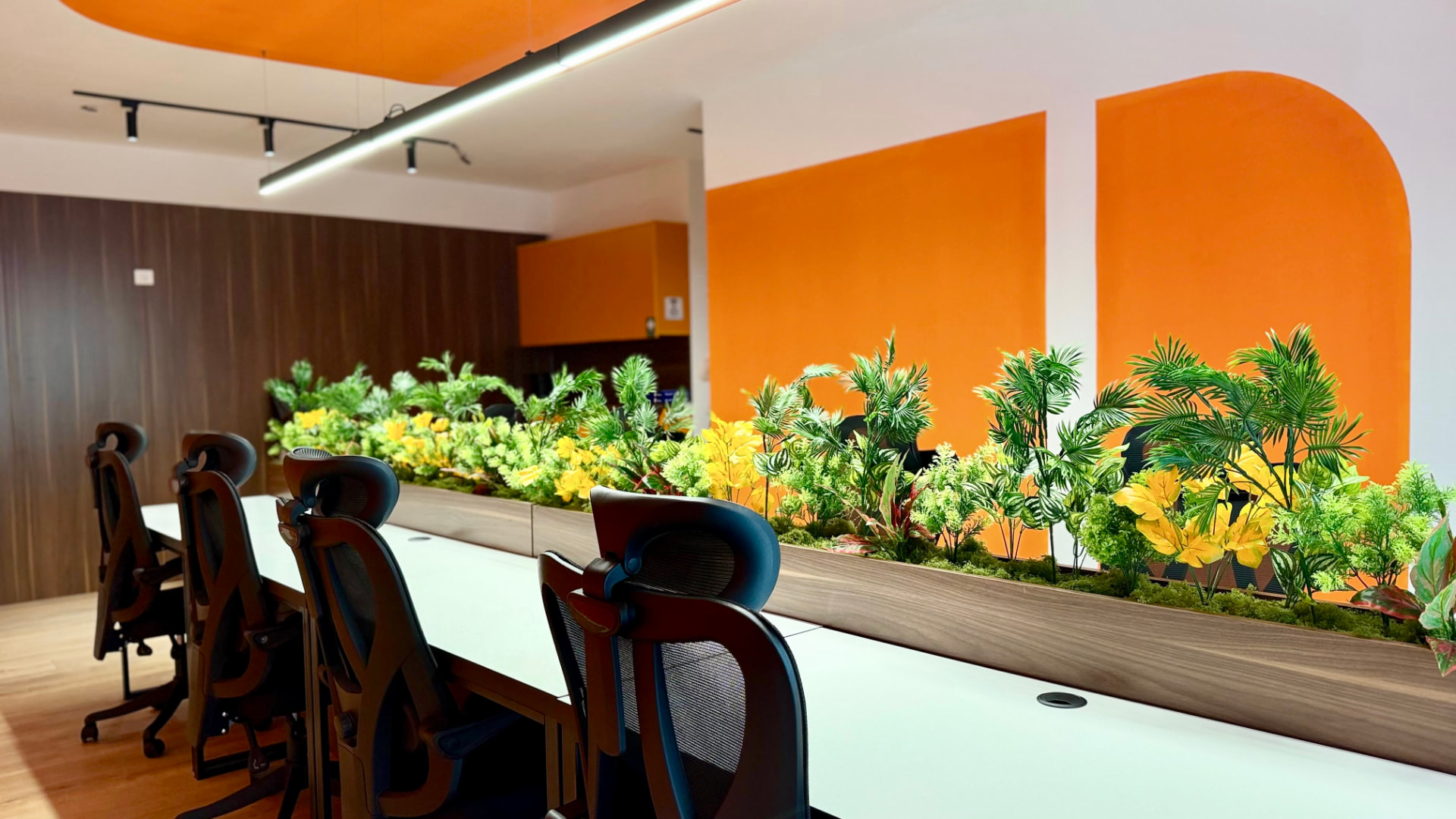 The main room at PRN Cowork: a long shared desk with a planter of flowers, orange walls and black office chairs
